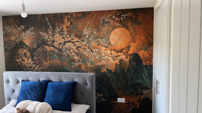 A bedroom with a grey bed, blue cushions, and a mural featuring a moonlit landscape.